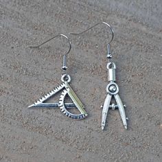 two pairs of silver earrings with scissors on top of them, sitting in the sand