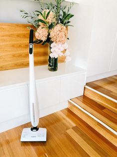 a white electric toothbrush sitting on top of a wooden floor next to a vase with flowers