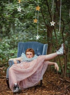 a woman in a pink dress is sitting on a blue chair with stars hanging from the ceiling