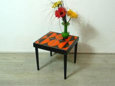 a vase with flowers sitting on top of a small table next to a white wall