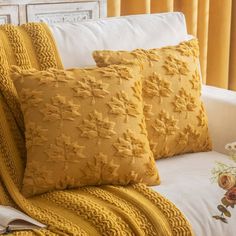 three yellow pillows on a bed with white linens and gold curtains behind the headboard