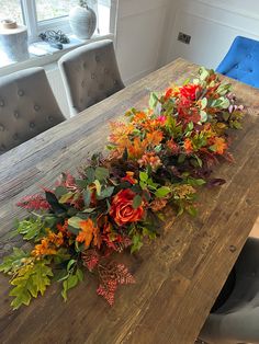 a wooden table topped with lots of flowers and greenery next to a blue chair