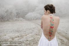 a woman with a tattoo on her back standing in a field full of frosty grass