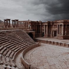 an ancient theater with stone steps and columns under a cloudy sky in the desert,