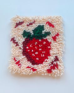 a red and white knitted square with a strawberry on the center, surrounded by small dots