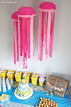 a table topped with cakes and desserts covered in pink tissue paper hanging from the ceiling