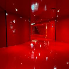 an empty room with red walls and flooring in the center is lit by lights