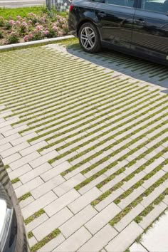 a black car parked on the side of a road next to a sidewalk with grass growing all over it