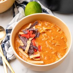 a bowl of soup with tortilla chips on top and a lime next to it