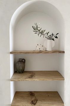 some shelves with vases and plants on them in a white walled room by the wall