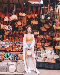 a woman standing in front of a market filled with baskets