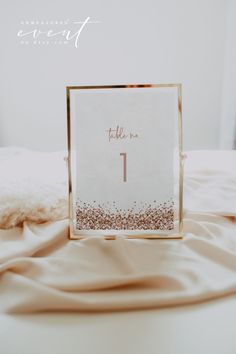 a table number is placed on top of a bed with a white sheet and gold frame