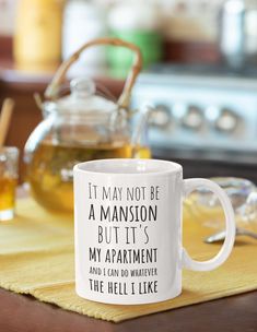 a white coffee mug sitting on top of a wooden table next to a tea pot