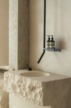 a white sink sitting next to a wall mounted faucet on a stone shelf