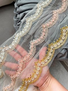 a woman's hand holding onto a veil with gold and white beads on it