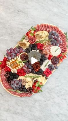 a platter filled with cheese, fruit and meats on top of a marble counter