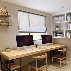 two computer monitors sitting on top of a wooden desk in front of a bookshelf