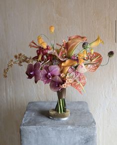 a vase filled with lots of colorful flowers on top of a cement block next to a wall