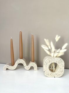 two candles are sitting next to each other on a shelf with some feathers in it