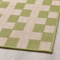 a green and white rug with squares on the floor in front of a wooden floor