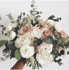 a hand holding a bouquet of white and pink flowers with greenery on the stems