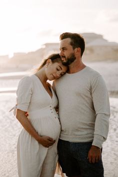 a pregnant couple standing next to each other on the beach