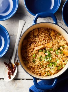 a pot filled with noodles and vegetables on top of blue plates next to spoons