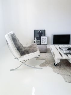 a living room with white furniture and a cowhide rug on the floor in front of two televisions