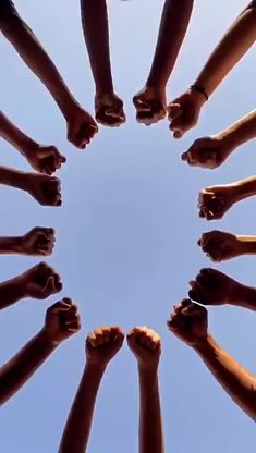 a group of people standing in a circle holding their hands together with the sky behind them