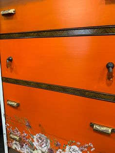 an orange dresser with flowers painted on the front and sides, along with brass handles