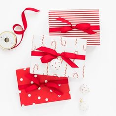 two red and white gift boxes with ribbons on them next to a spool of thread