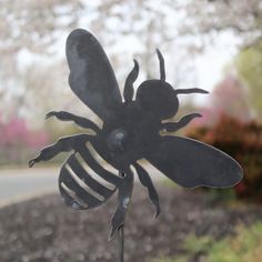 a metal bee sculpture sitting on top of a wooden post in front of a tree