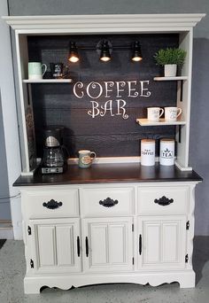 a coffee bar with white cabinets and black counter tops is displayed in a room that has gray walls