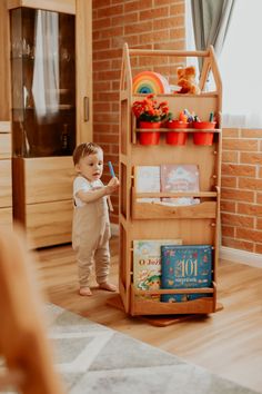 a toddler standing in front of a bookcase with books on it and holding a toothbrush