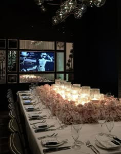 a long table is set with wine glasses and place settings in front of a television