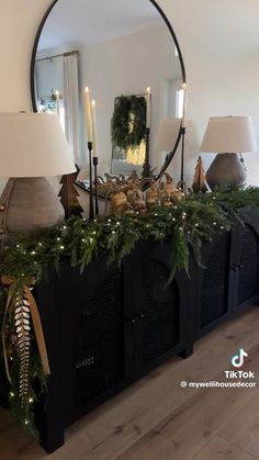 a table with christmas decorations and lights on it in front of a large round mirror