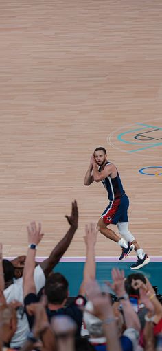 a basketball player is jumping in the air with his hands up and people are clapping around him