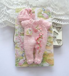 a pink knitted baby's footie laying on top of a lace doily