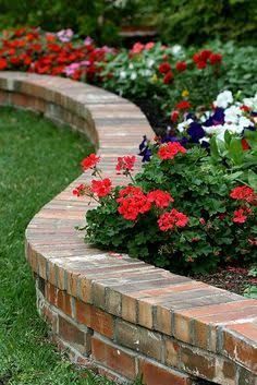 an image of a flower bed with brick edging and flowers in the back ground