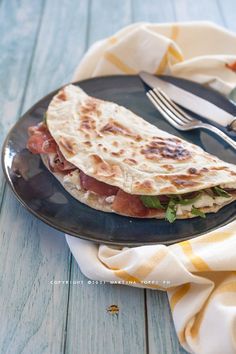 a black plate topped with a quesadilla next to a fork and knife