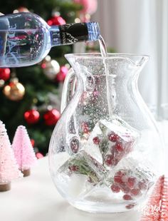 a glass pitcher filled with ice and cranberries on top of a table next to a christmas tree