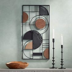 a table topped with a wooden bowl next to a candle holder and metal wall art