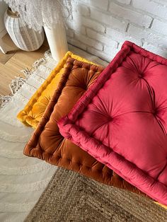 three different colored cushions on the floor next to a white brick wall and rugs