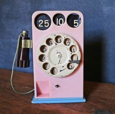 an old fashioned pink phone sitting on top of a wooden table next to a coin