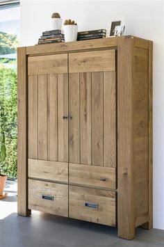 a large wooden cabinet with drawers in front of a window and potted plant on top