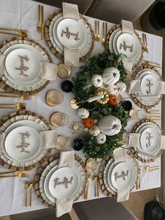 a table set for thanksgiving dinner with white and gold plates, pumpkins and greenery