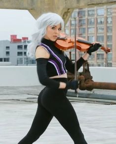 a woman with white hair is playing the violin on top of a roof in an urban setting