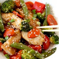 a white plate topped with chicken and veggies covered in sesame seed sauce on top of broccoli