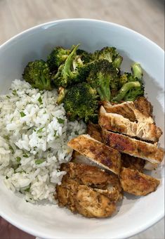 a white bowl filled with rice and meat next to broccoli on a table