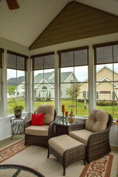 two wicker chairs sitting on top of a rug in front of large windows with brown shades